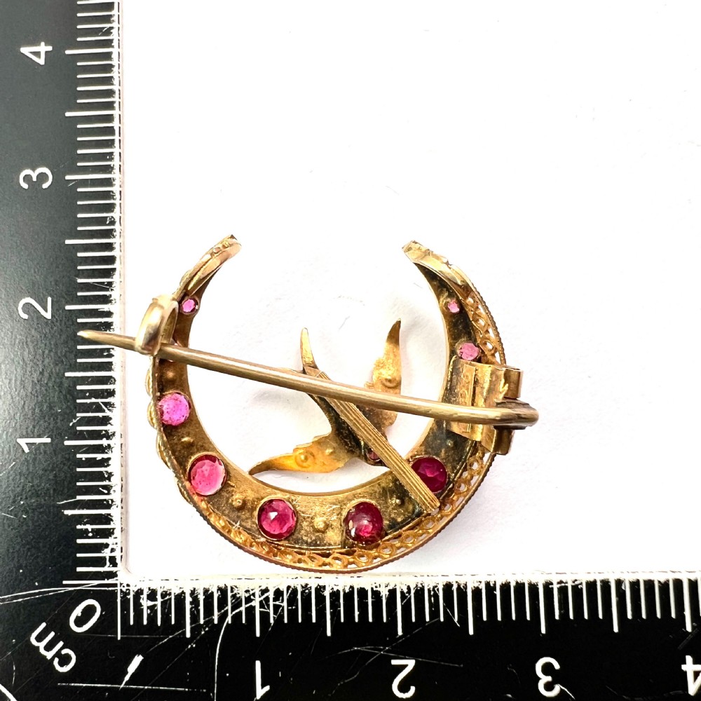 A 9ct gold crescent moon brooch set with alternating rubies and seed pearls surrounding a central swallow motif embellished with pearls and a ruby eye. View VII