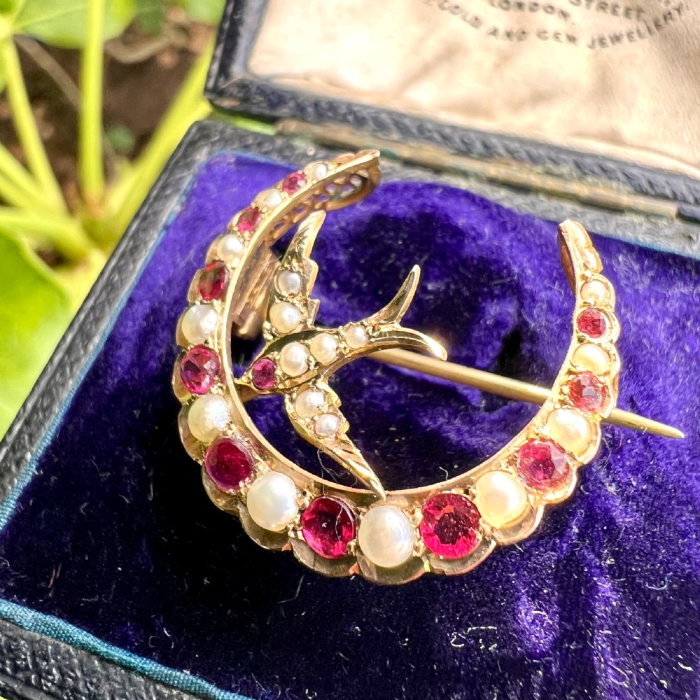 A 9ct gold crescent moon brooch set with alternating rubies and seed pearls surrounding a central swallow motif embellished with pearls and a ruby eye. View VIII