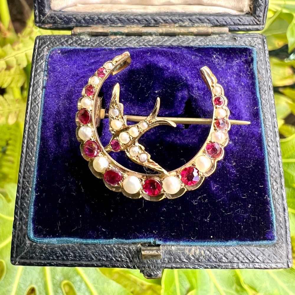 A 9ct gold crescent moon brooch set with alternating rubies and seed pearls surrounding a central swallow motif embellished with pearls and a ruby eye. View IX