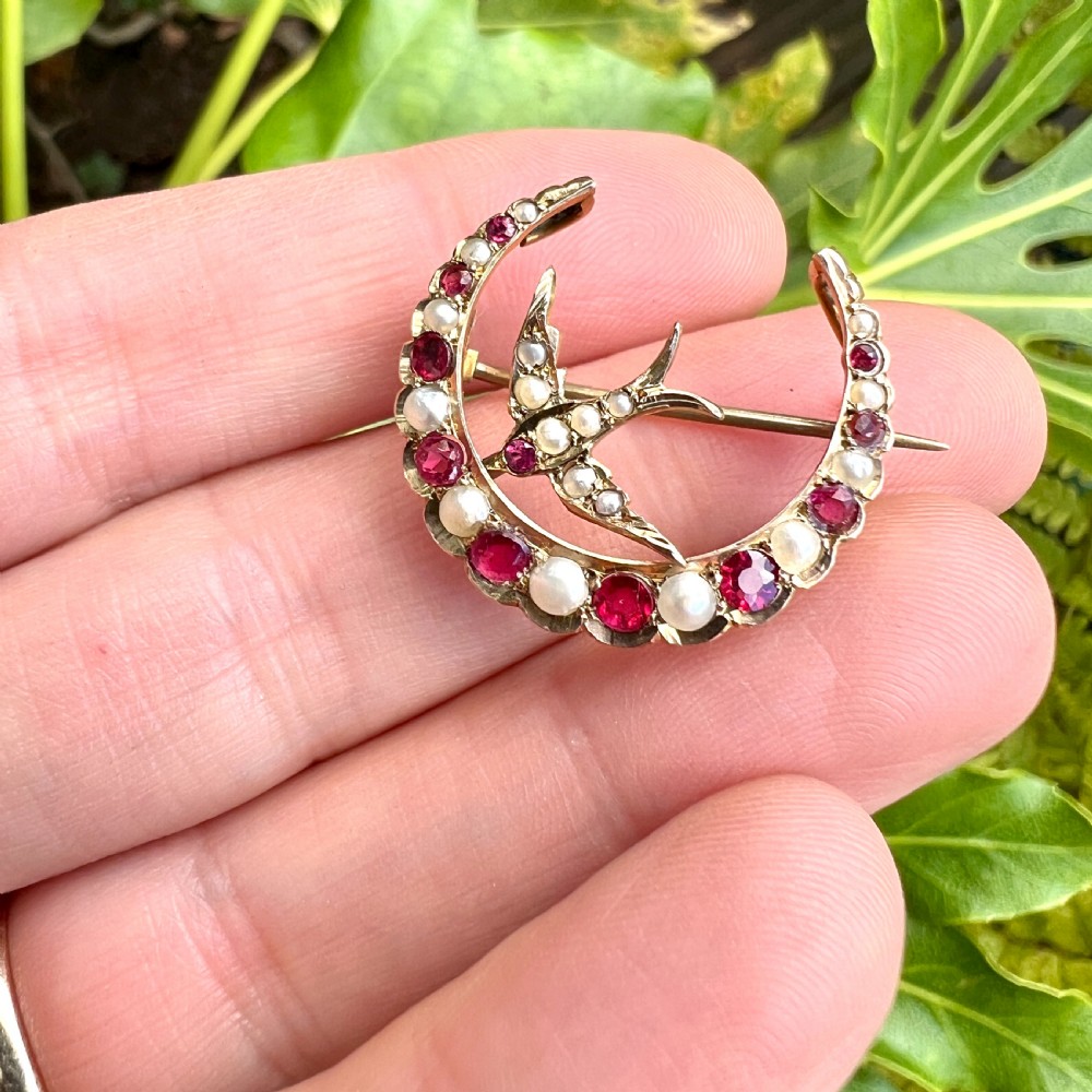 A 9ct gold crescent moon brooch set with alternating rubies and seed pearls surrounding a central swallow motif embellished with pearls and a ruby eye. View X