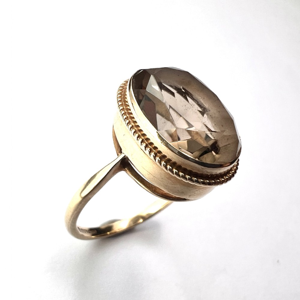 A vintage yellow gold ring set with a large oval faceted translucent brown smoky quartz stone framed by a twisted rope bezel detail.