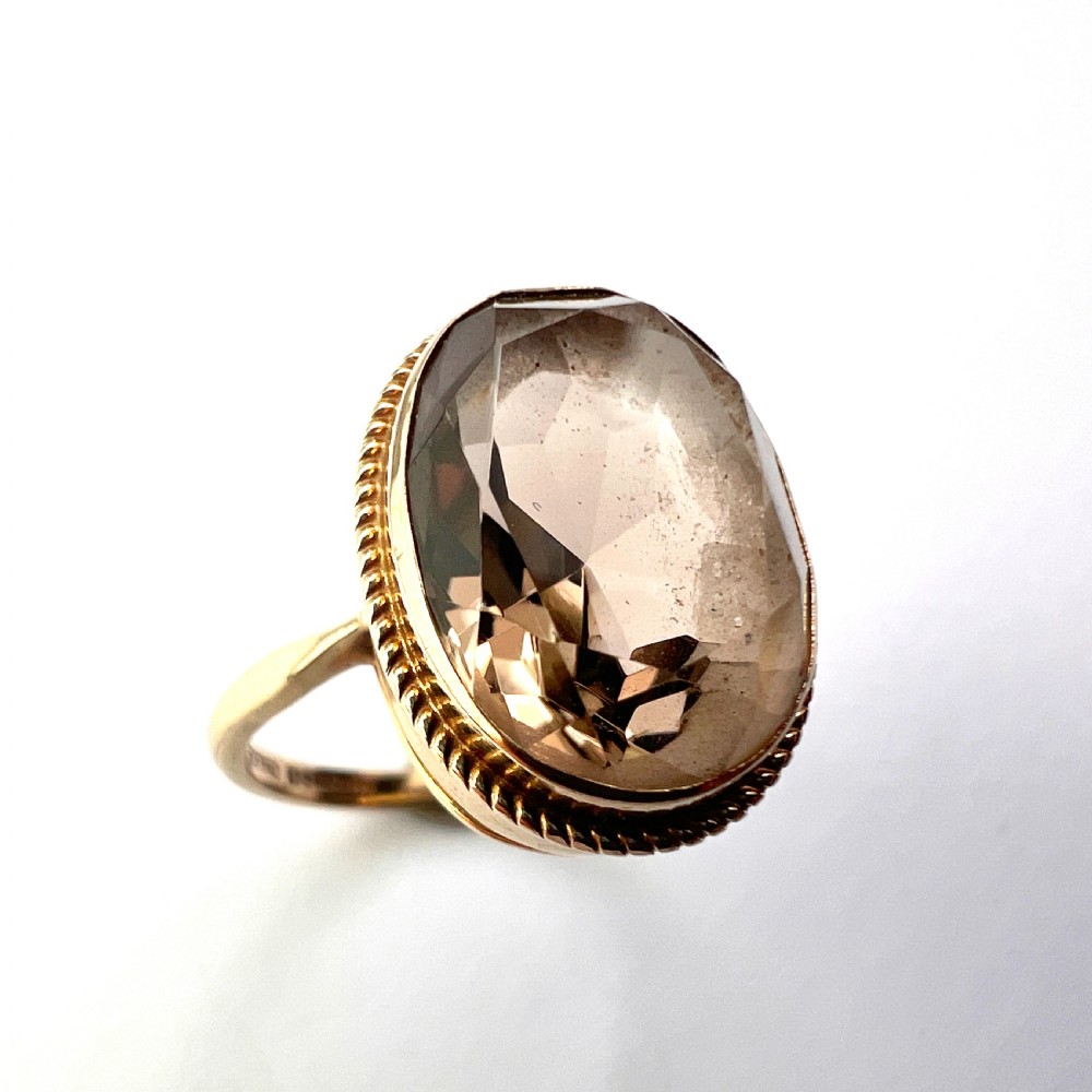 A vintage yellow gold ring set with a large oval faceted translucent brown smoky quartz stone framed by a twisted rope bezel detail. View II