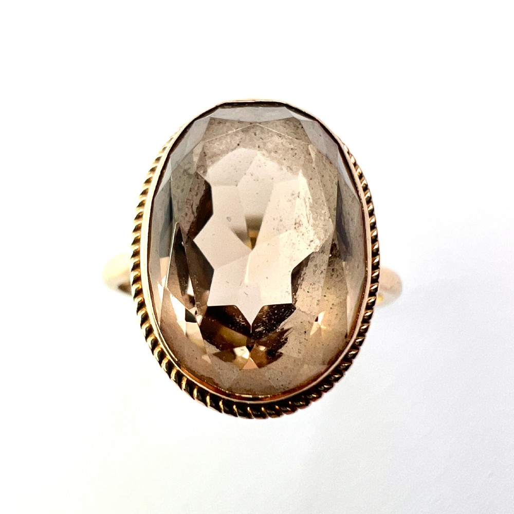A vintage yellow gold ring set with a large oval faceted translucent brown smoky quartz stone framed by a twisted rope bezel detail. View III