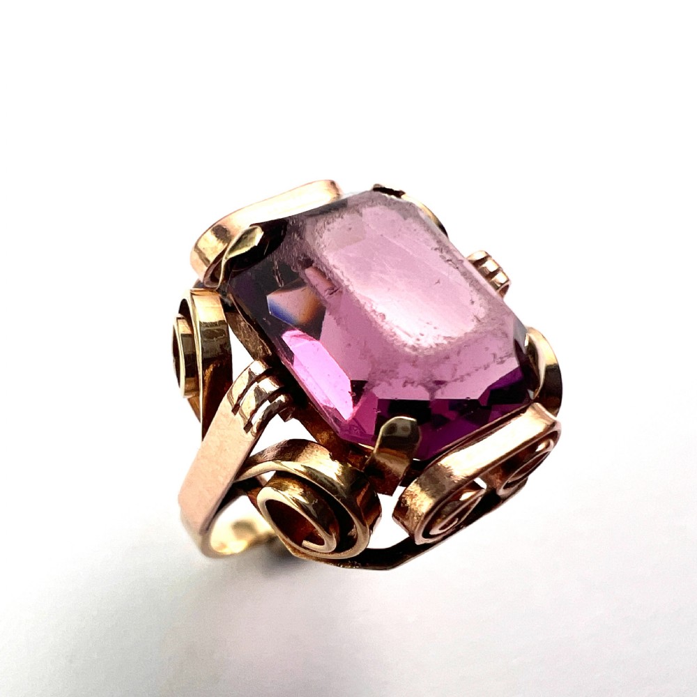 A 1940s Retro 14ct gold cocktail ring featuring a large rectangular cut purple paste gemstone set within ornate metal scrollwork. View III