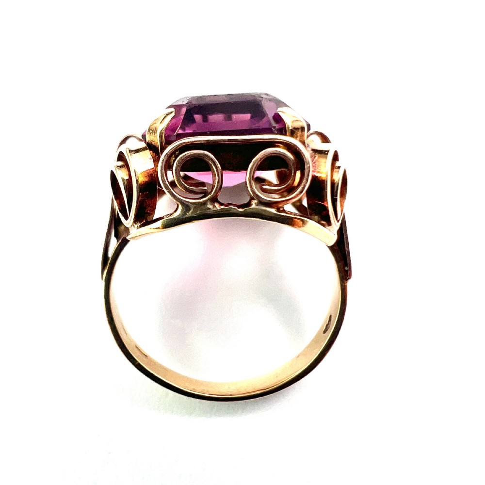 A 1940s Retro 14ct gold cocktail ring featuring a large rectangular cut purple paste gemstone set within ornate metal scrollwork. View V