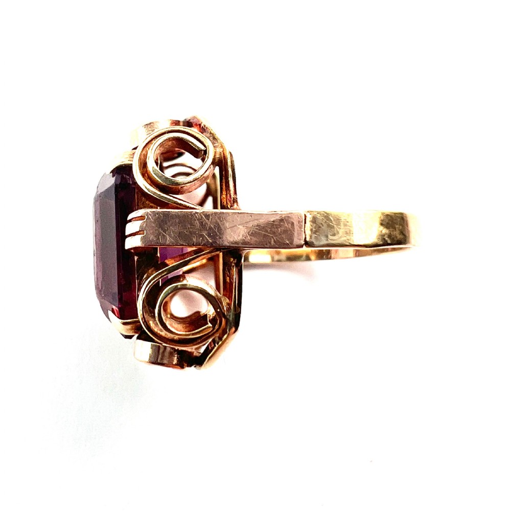 A 1940s Retro 14ct gold cocktail ring featuring a large rectangular cut purple paste gemstone set within ornate metal scrollwork. View VI