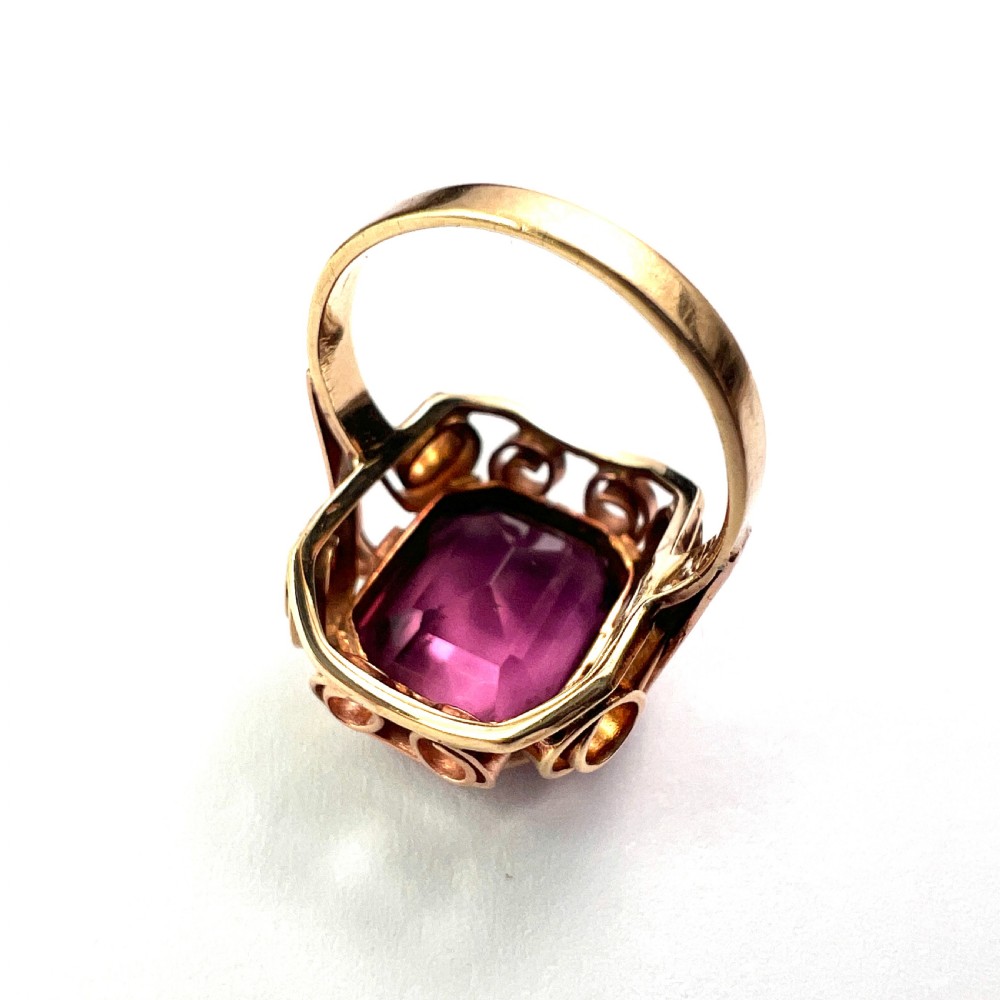 A 1940s Retro 14ct gold cocktail ring featuring a large rectangular cut purple paste gemstone set within ornate metal scrollwork. View VIII