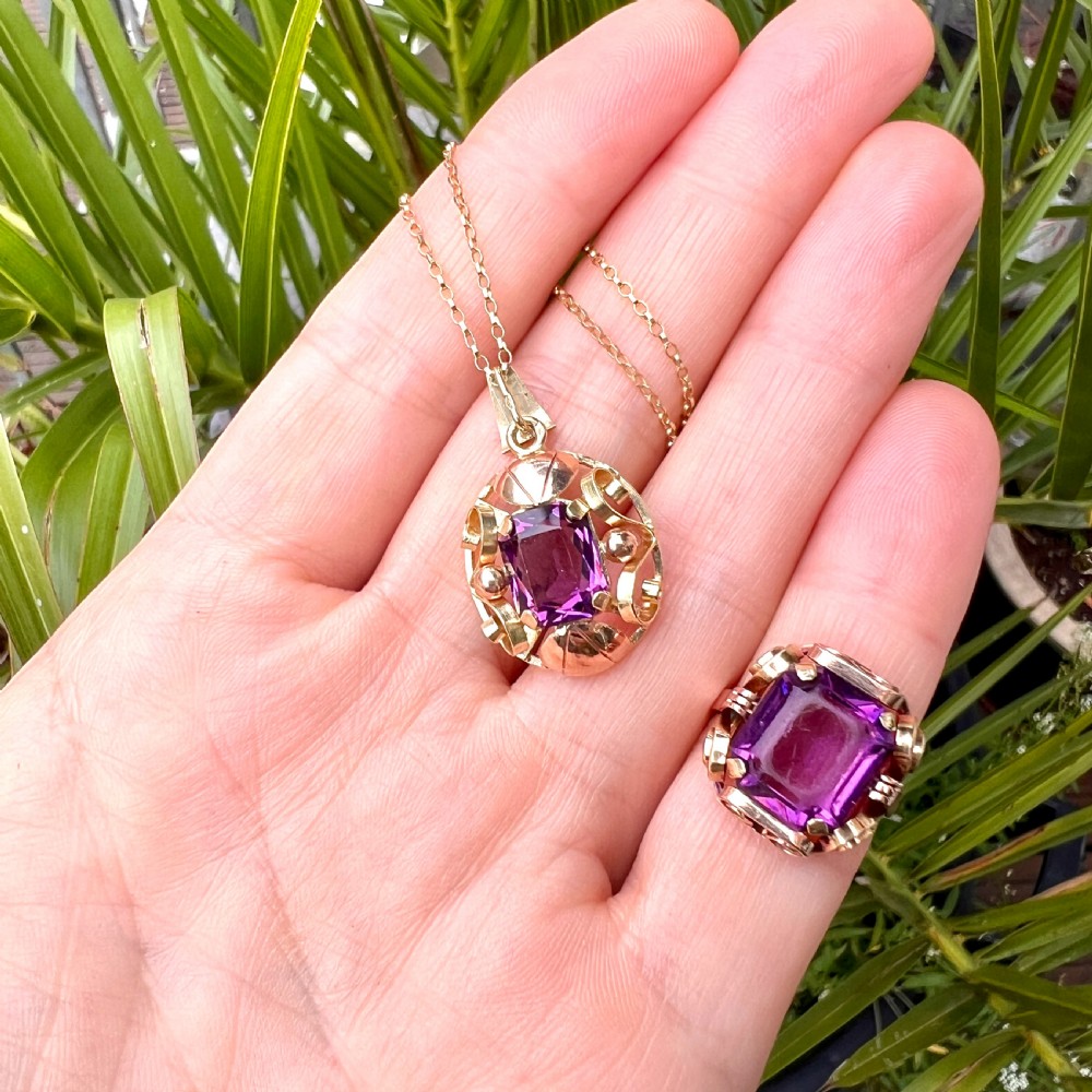 A 1940s Retro 14ct gold cocktail ring featuring a large rectangular cut purple paste gemstone set within ornate metal scrollwork. View X