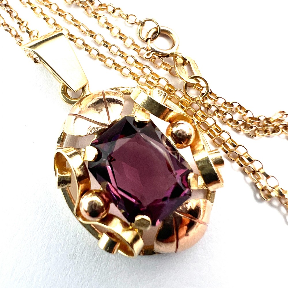 A 14ct yellow gold 1940s pendant featuring a central emerald-cut purple paste stone framed by sculptural gold scrolls and sphere accents.