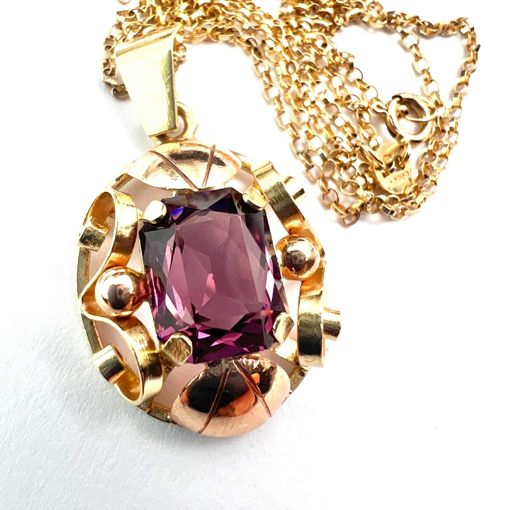 A 14ct yellow gold 1940s pendant featuring a central emerald-cut purple paste stone framed by sculptural gold scrolls and sphere accents. View II