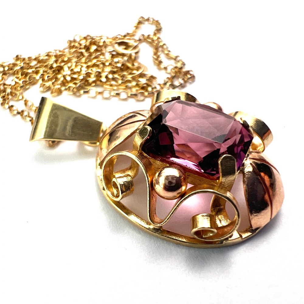 A 14ct yellow gold 1940s pendant featuring a central emerald-cut purple paste stone framed by sculptural gold scrolls and sphere accents. View III