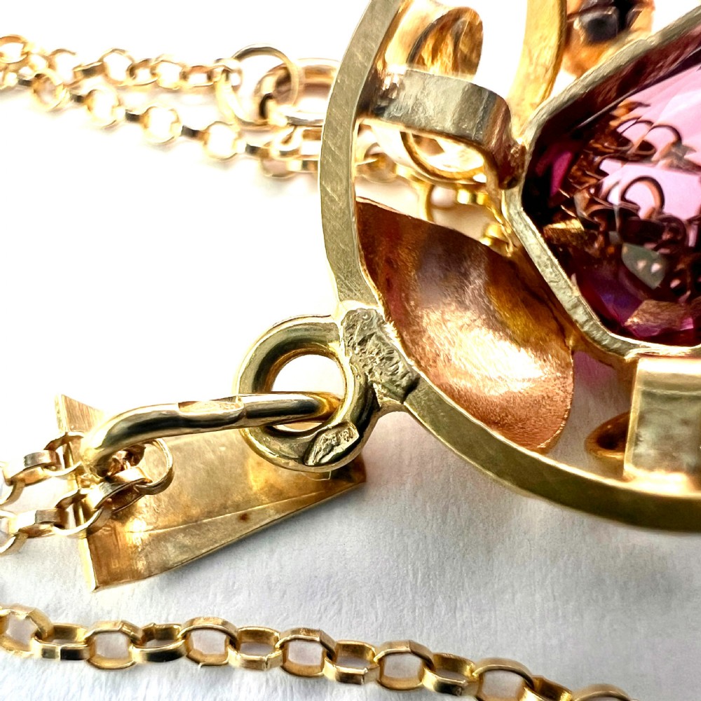 A 14ct yellow gold 1940s pendant featuring a central emerald-cut purple paste stone framed by sculptural gold scrolls and sphere accents. View VII