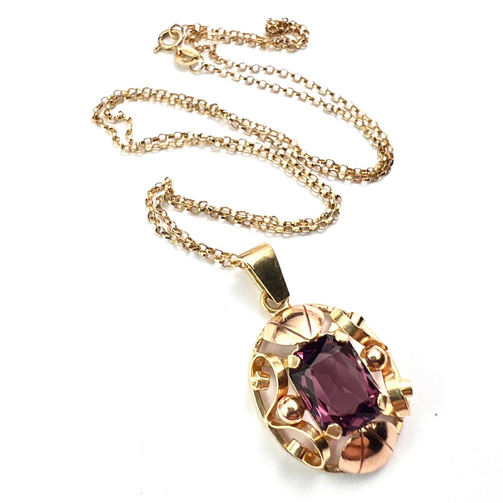 A 14ct yellow gold 1940s pendant featuring a central emerald-cut purple paste stone framed by sculptural gold scrolls and sphere accents. View VIII