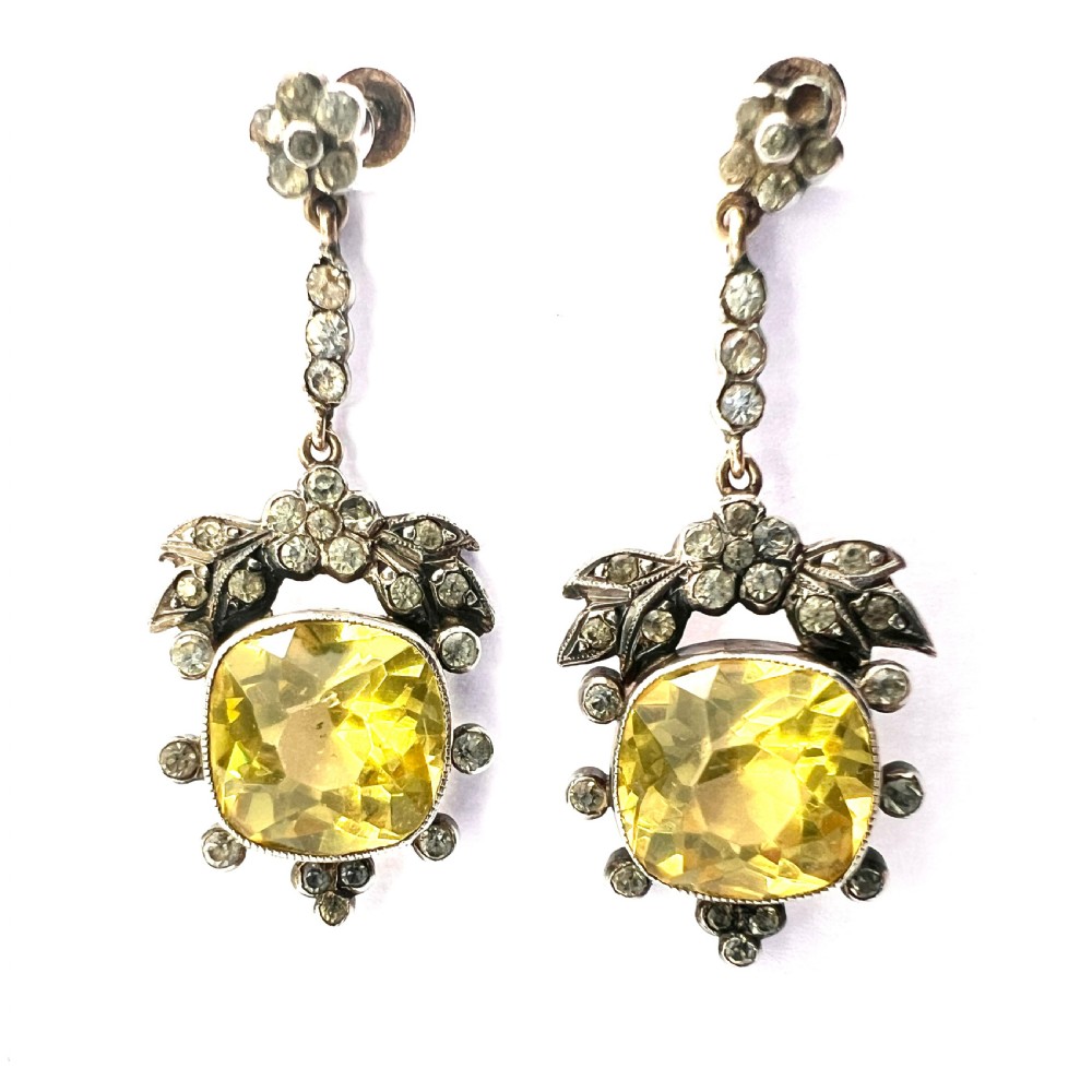 A pair of Victorian silver drop earrings featuring cushion-cut yellow citrine paste stones surrounded by foliate settings with clear glass accents.