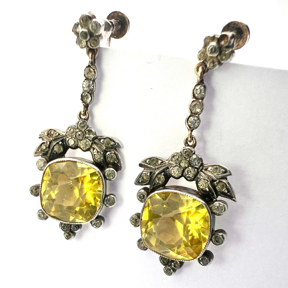 A pair of Victorian silver drop earrings featuring cushion-cut yellow citrine paste stones surrounded by foliate settings with clear glass accents. View II
