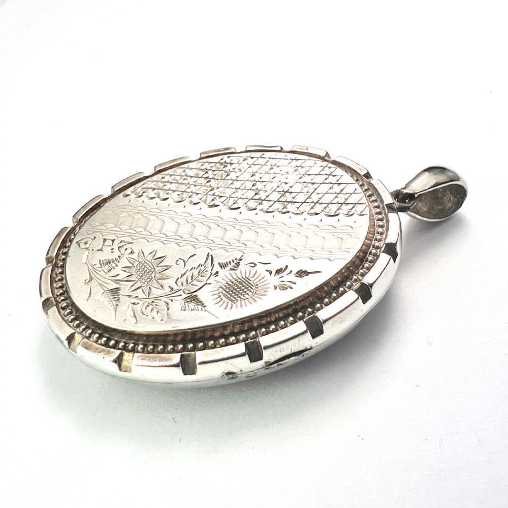 An oval Victorian silver locket decorated with intricate floral engraving, geometric crosshatching, and a beaded border. View II