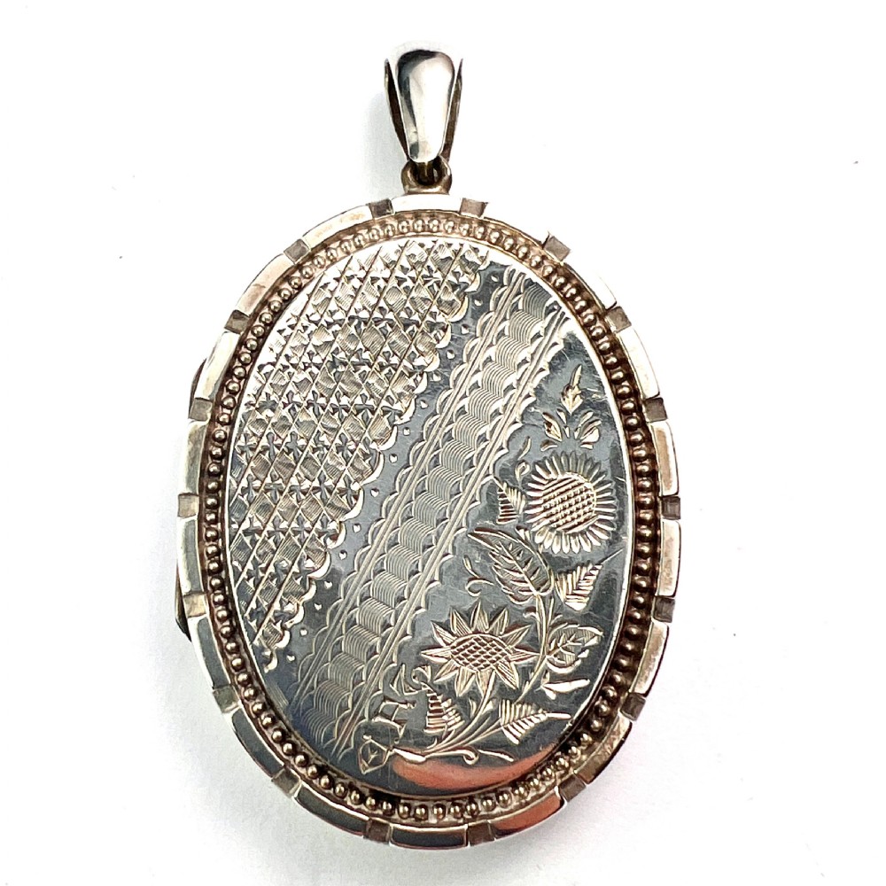An oval Victorian silver locket decorated with intricate floral engraving, geometric crosshatching, and a beaded border. View III