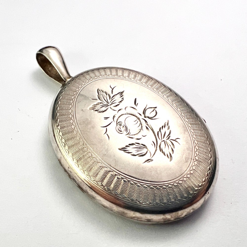 An oval Victorian silver locket decorated with intricate floral engraving, geometric crosshatching, and a beaded border. View IV