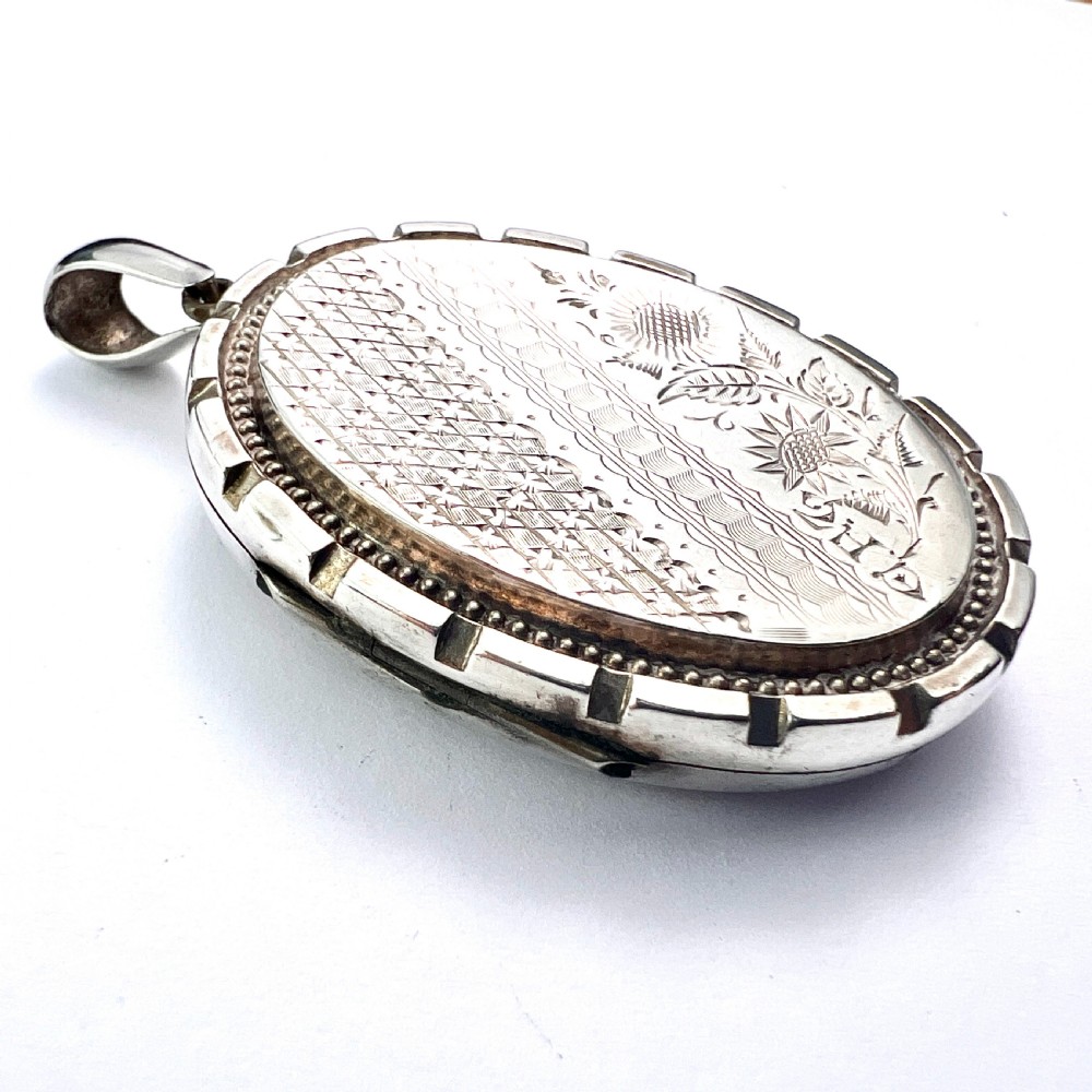 An oval Victorian silver locket decorated with intricate floral engraving, geometric crosshatching, and a beaded border. View V