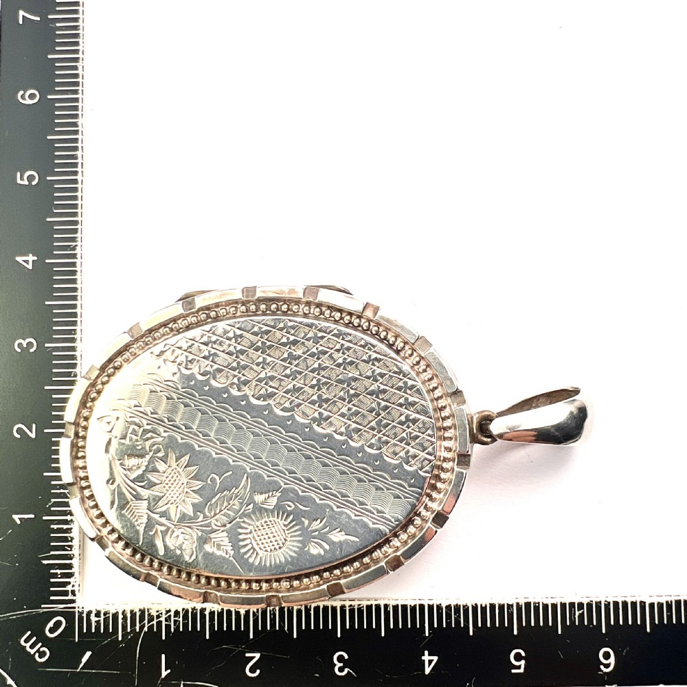 An oval Victorian silver locket decorated with intricate floral engraving, geometric crosshatching, and a beaded border. View VI