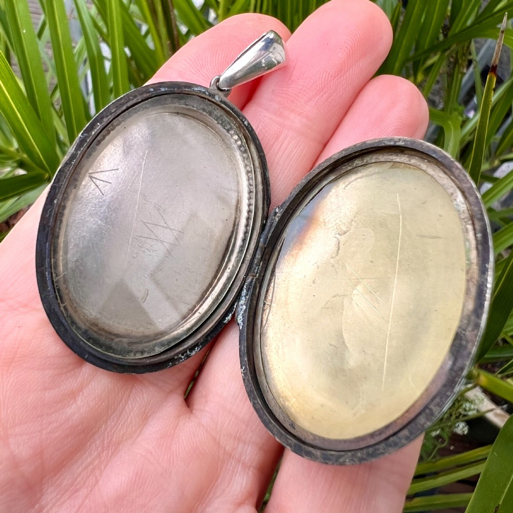 An oval Victorian silver locket decorated with intricate floral engraving, geometric crosshatching, and a beaded border. View VII