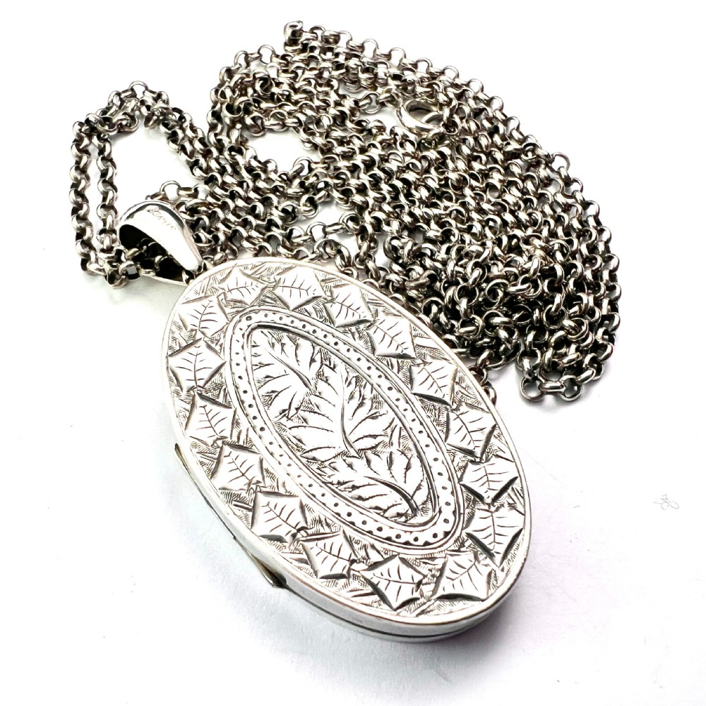 A large Victorian oval sterling silver locket with intricate foliate engraving, attached to a heavy belcher chain.