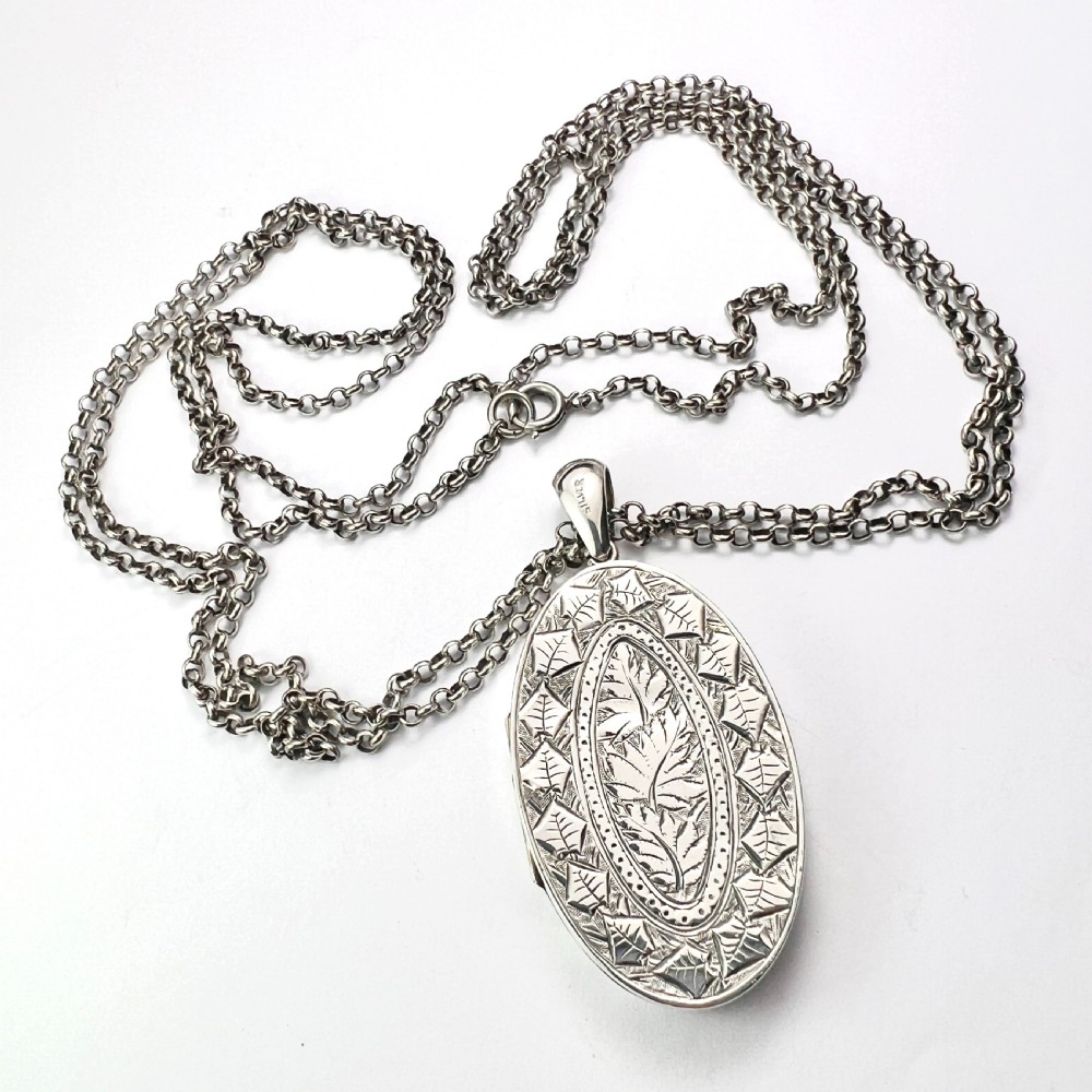 A large Victorian oval sterling silver locket with intricate foliate engraving, attached to a heavy belcher chain. View II