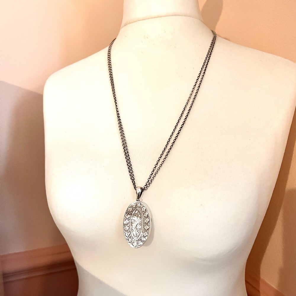 A large Victorian oval sterling silver locket with intricate foliate engraving, attached to a heavy belcher chain. View V