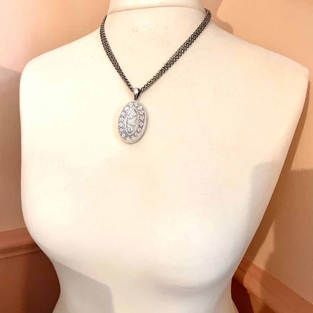 A large Victorian oval sterling silver locket with intricate foliate engraving, attached to a heavy belcher chain. View VI