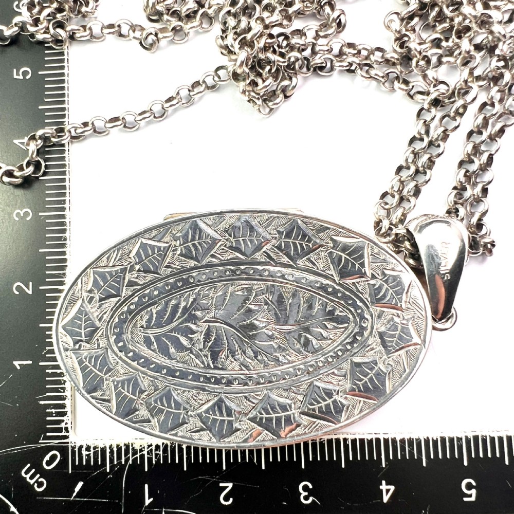 A large Victorian oval sterling silver locket with intricate foliate engraving, attached to a heavy belcher chain. View VIII