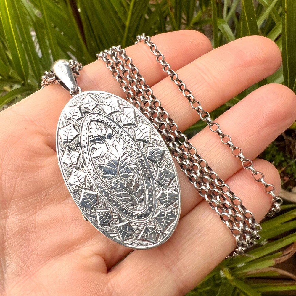A large Victorian oval sterling silver locket with intricate foliate engraving, attached to a heavy belcher chain. View IX