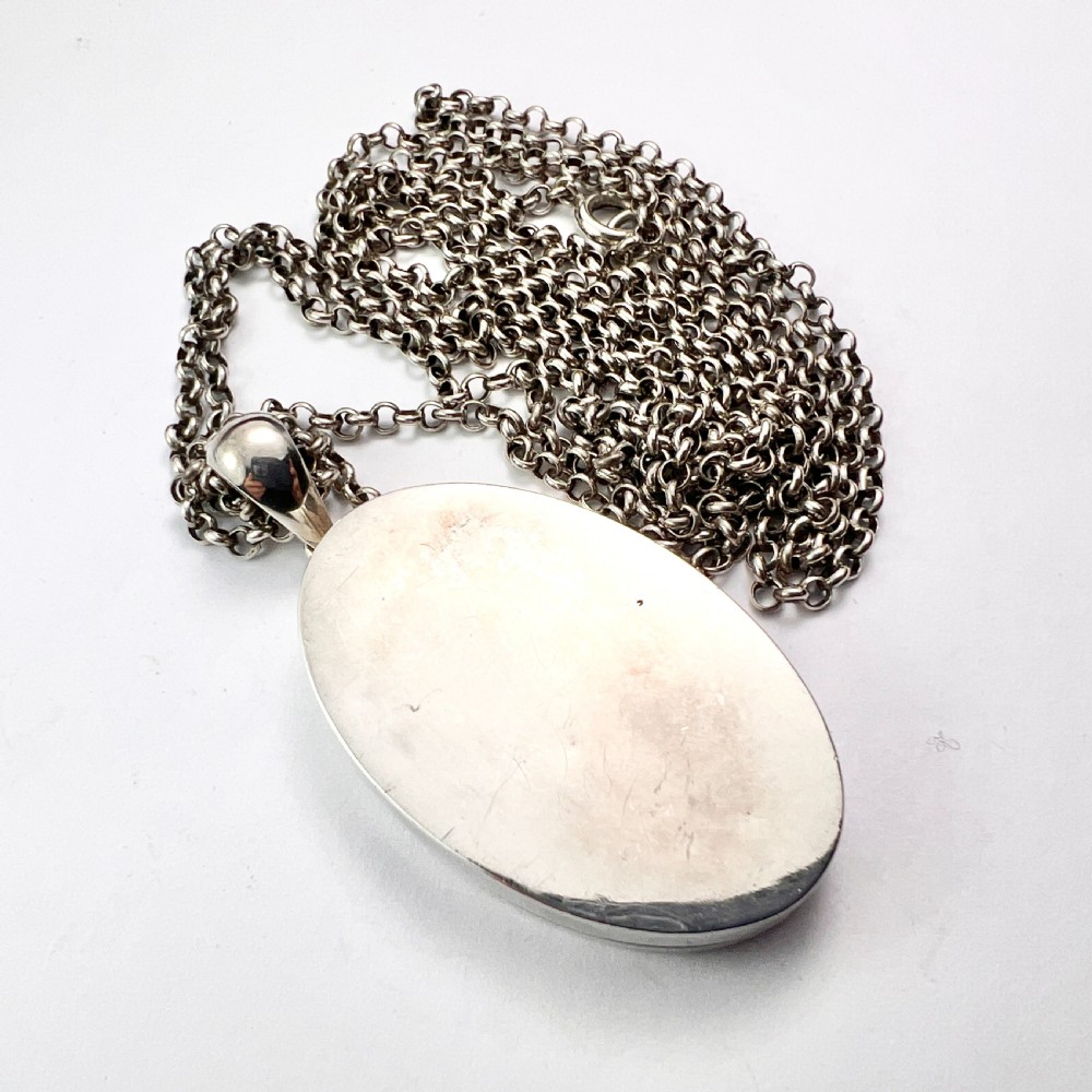 A large Victorian oval sterling silver locket with intricate foliate engraving, attached to a heavy belcher chain. View X