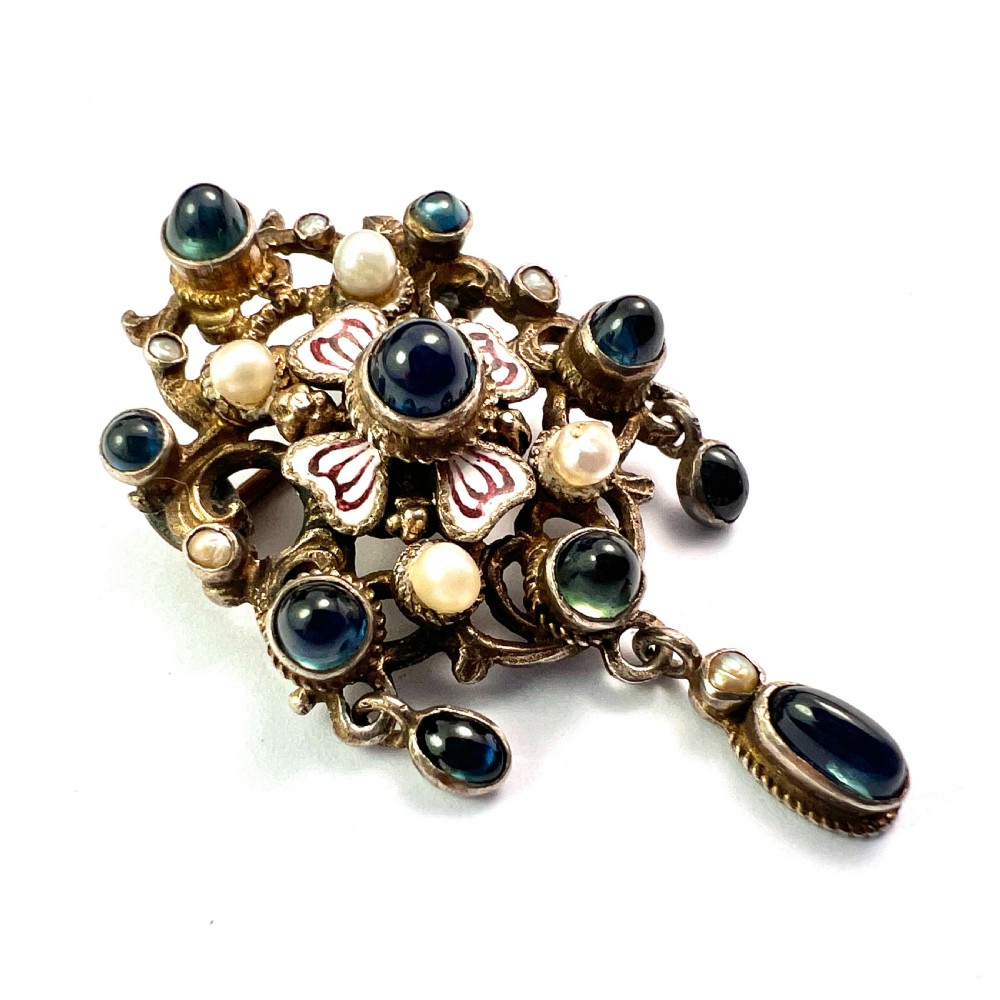 An Austro-Hungarian silver-gilt brooch decorated with blue cabochons, seed pearls, polychrome enamel, and a dangling teardrop pendant. View V
