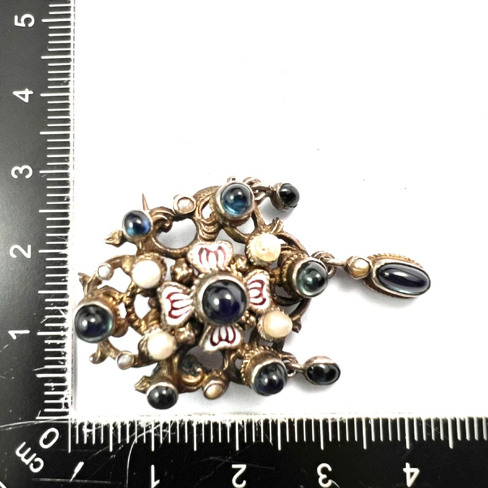 An Austro-Hungarian silver-gilt brooch decorated with blue cabochons, seed pearls, polychrome enamel, and a dangling teardrop pendant. View VII