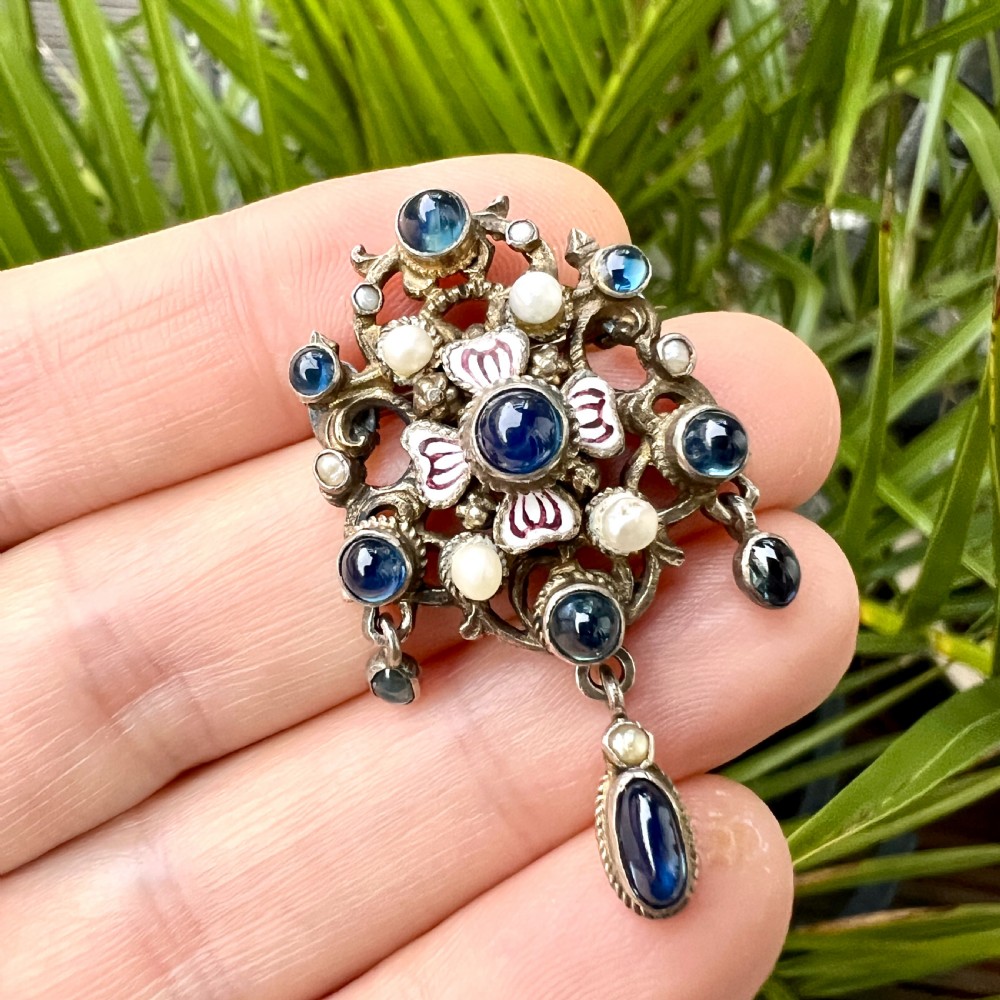 An Austro-Hungarian silver-gilt brooch decorated with blue cabochons, seed pearls, polychrome enamel, and a dangling teardrop pendant. View VIII