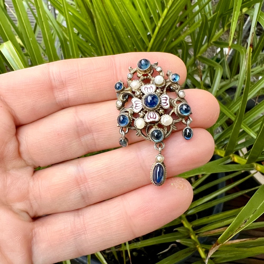 An Austro-Hungarian silver-gilt brooch decorated with blue cabochons, seed pearls, polychrome enamel, and a dangling teardrop pendant. View IX