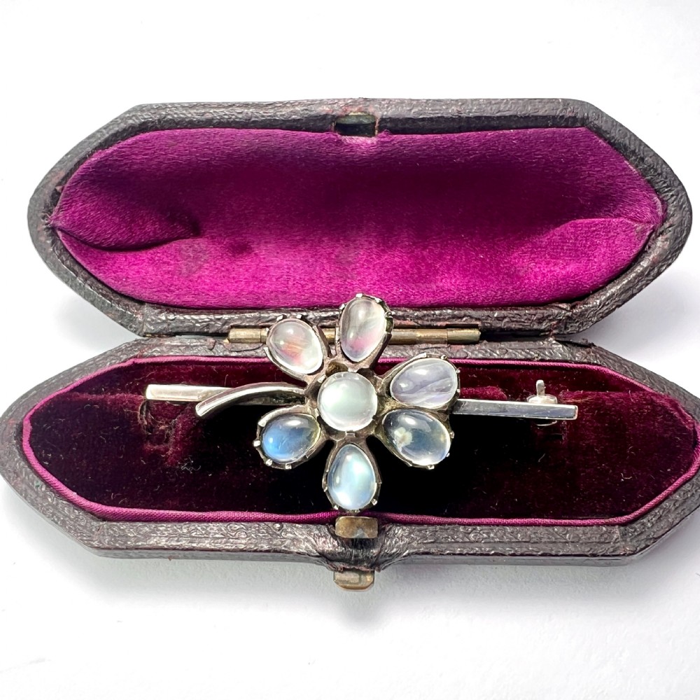 An antique silver bar brooch featuring a central flower design set with six teardrop-shaped and one round cabochon moonstone.