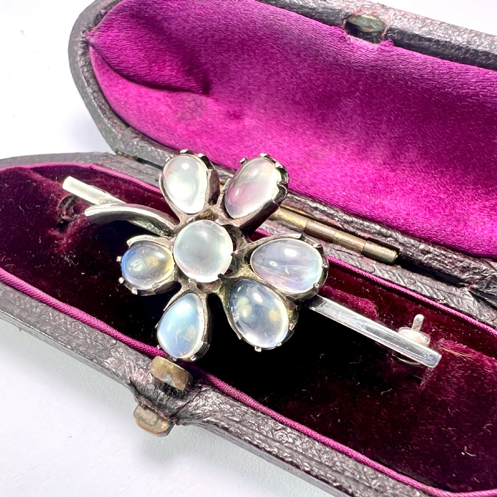 An antique silver bar brooch featuring a central flower design set with six teardrop-shaped and one round cabochon moonstone. View II