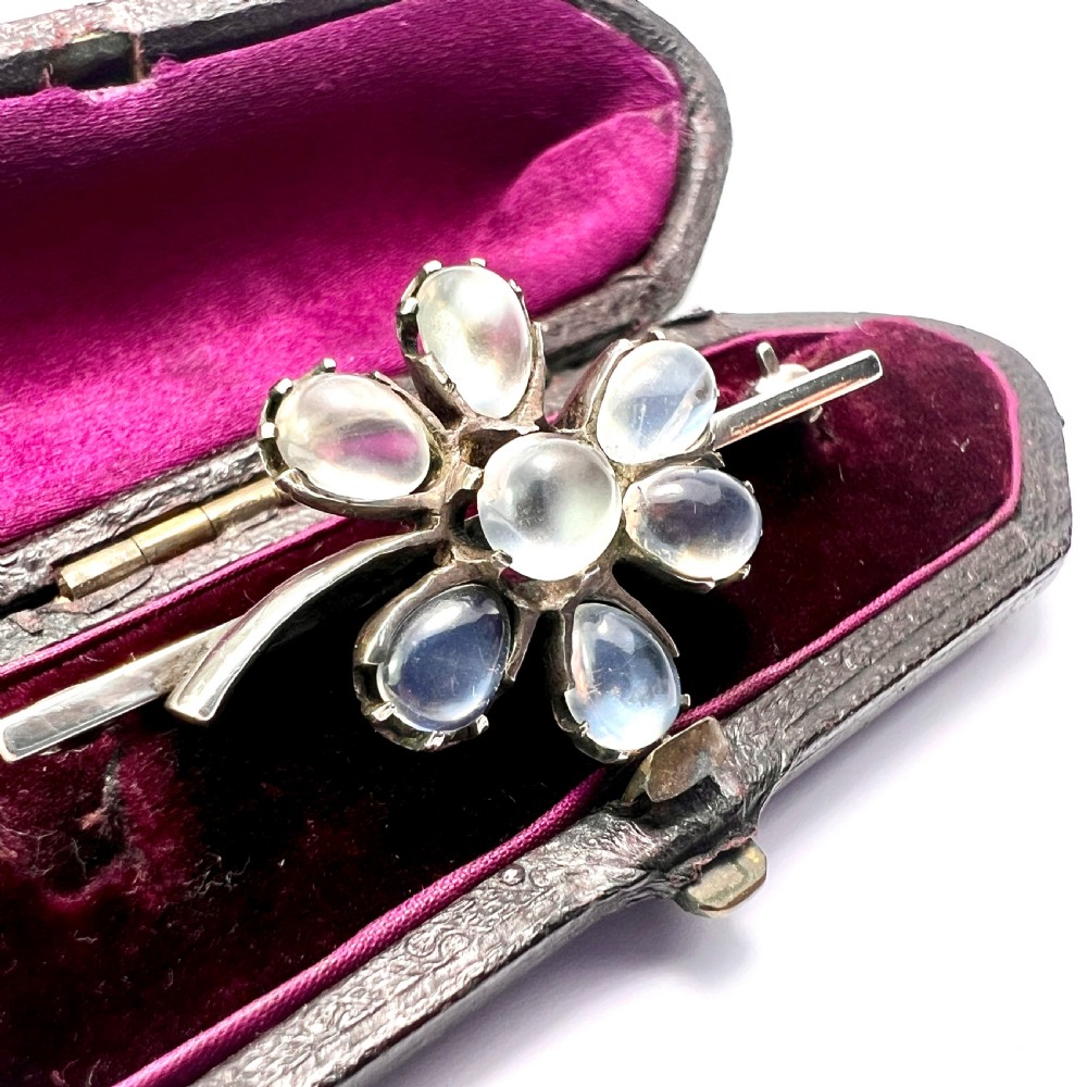 An antique silver bar brooch featuring a central flower design set with six teardrop-shaped and one round cabochon moonstone. View III