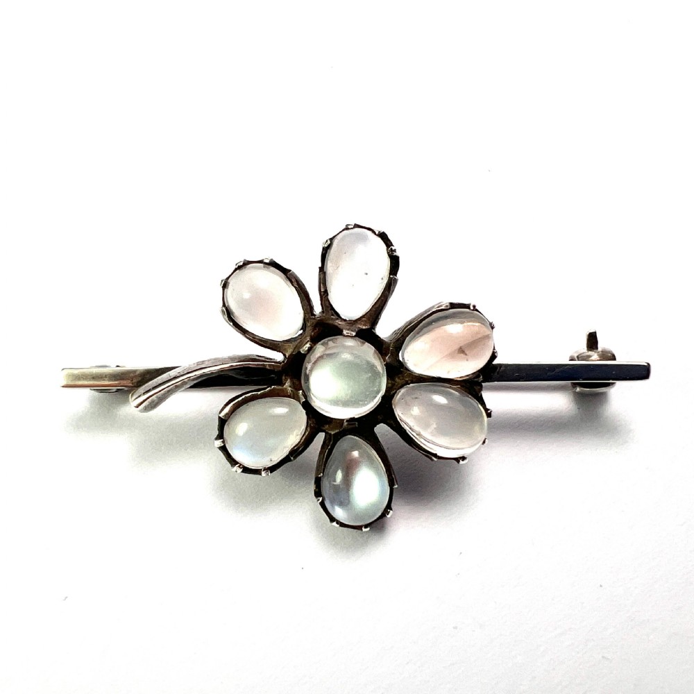 An antique silver bar brooch featuring a central flower design set with six teardrop-shaped and one round cabochon moonstone. View IV