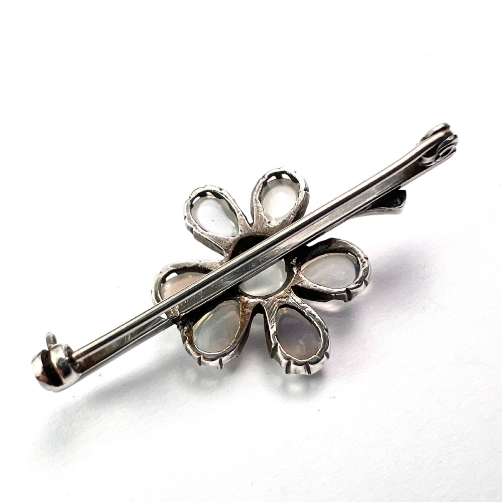 An antique silver bar brooch featuring a central flower design set with six teardrop-shaped and one round cabochon moonstone. View V