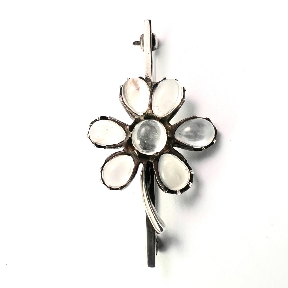 An antique silver bar brooch featuring a central flower design set with six teardrop-shaped and one round cabochon moonstone. View VI