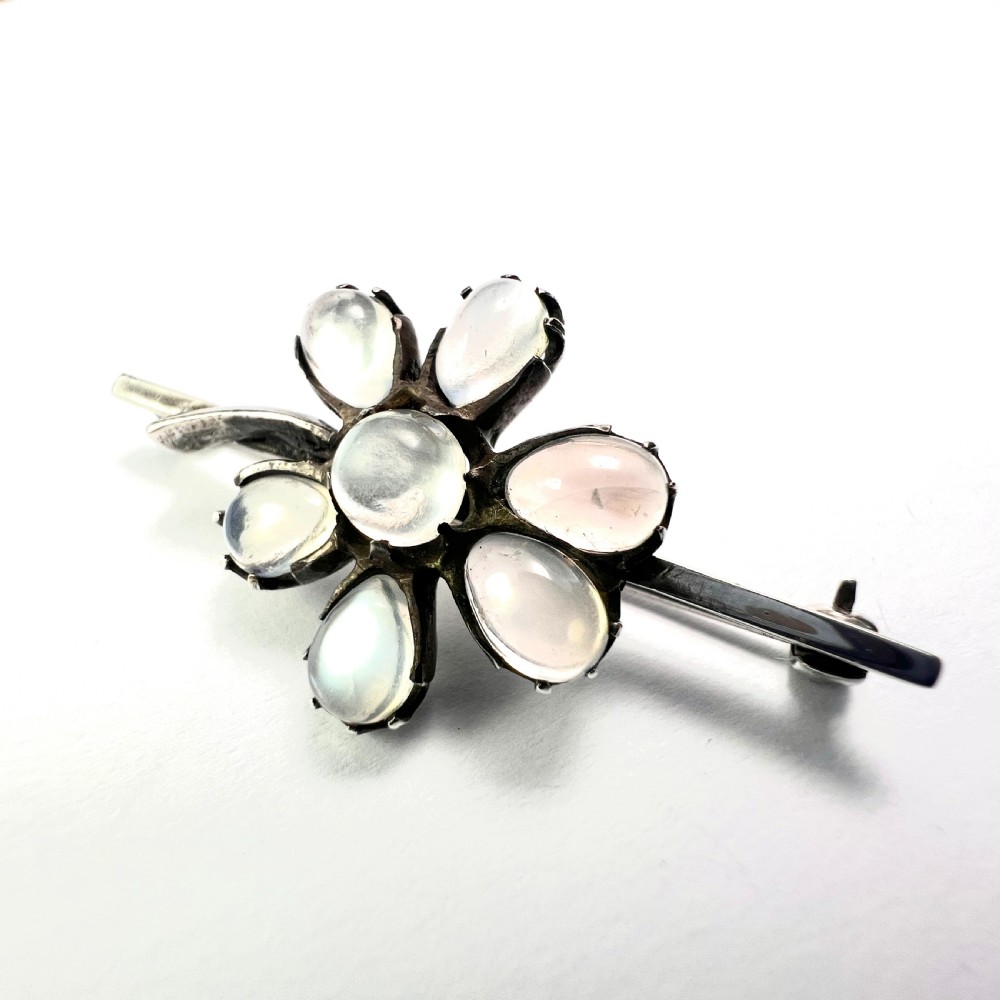 An antique silver bar brooch featuring a central flower design set with six teardrop-shaped and one round cabochon moonstone. View VII