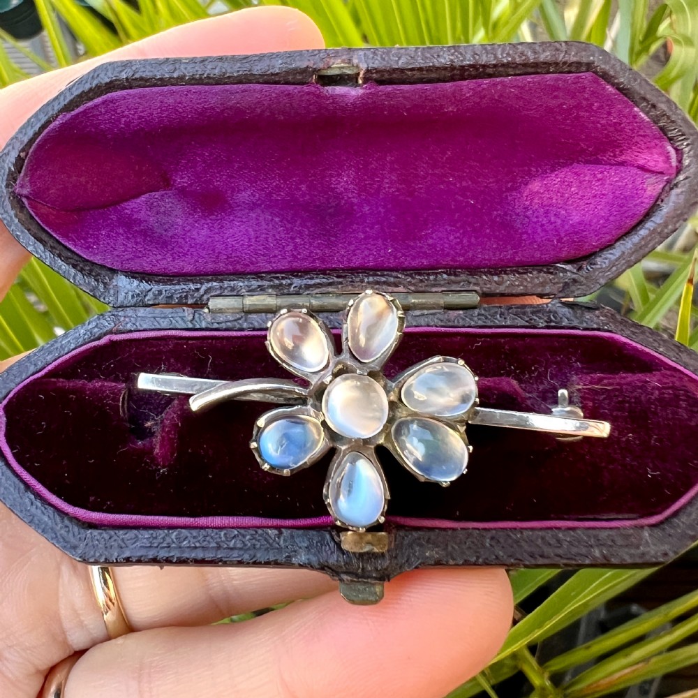 An antique silver bar brooch featuring a central flower design set with six teardrop-shaped and one round cabochon moonstone. View VIII