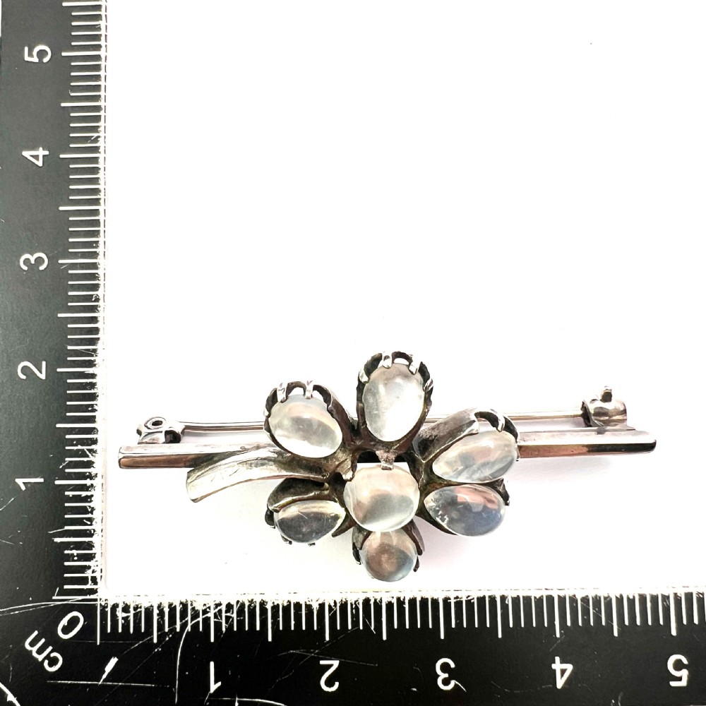 An antique silver bar brooch featuring a central flower design set with six teardrop-shaped and one round cabochon moonstone. View IX