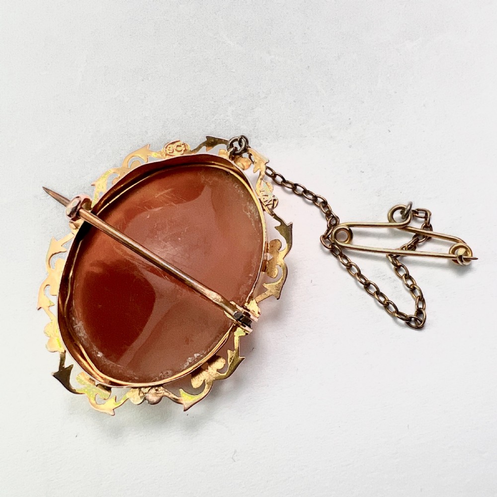 An oval Victorian 9ct gold brooch featuring a white carved shell cameo of a classical female profile set within an ornate openwork scroll frame with an attached safety pin. View IX