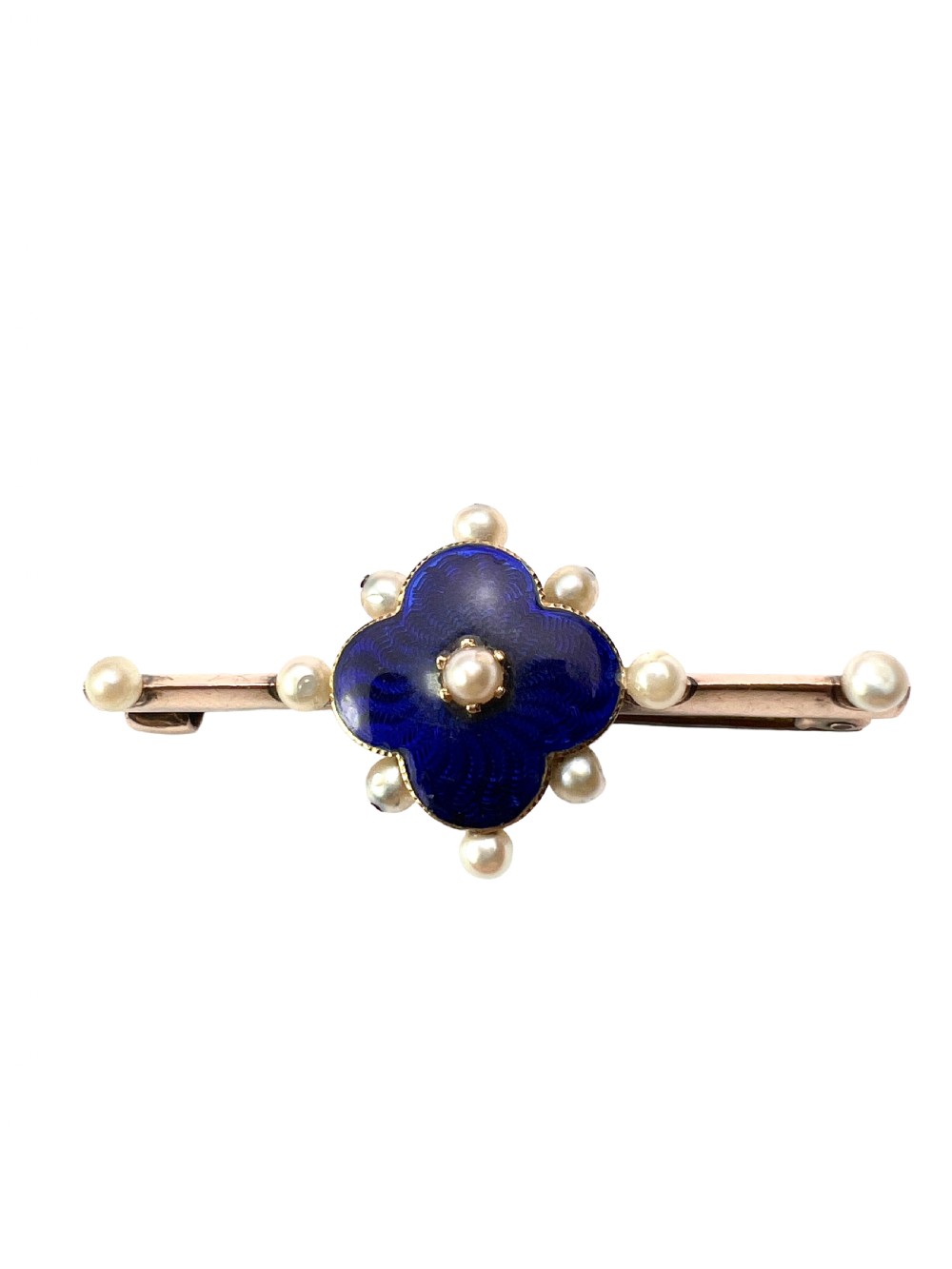 An Edwardian gold bar brooch featuring a central quatrefoil motif decorated in cobalt blue guilloche enamel and surrounded by pearls.