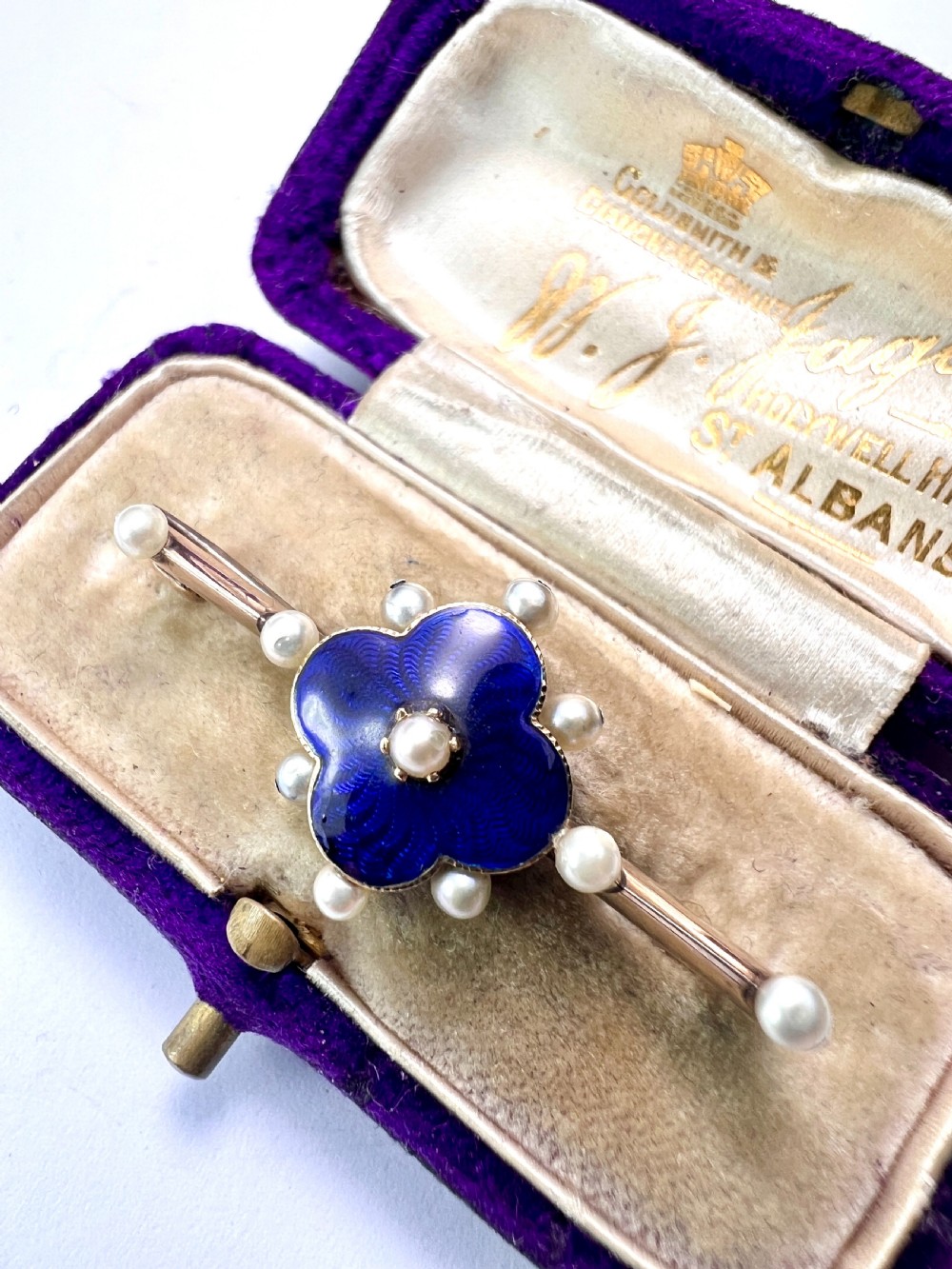 An Edwardian gold bar brooch featuring a central quatrefoil motif decorated in cobalt blue guilloche enamel and surrounded by pearls. View III