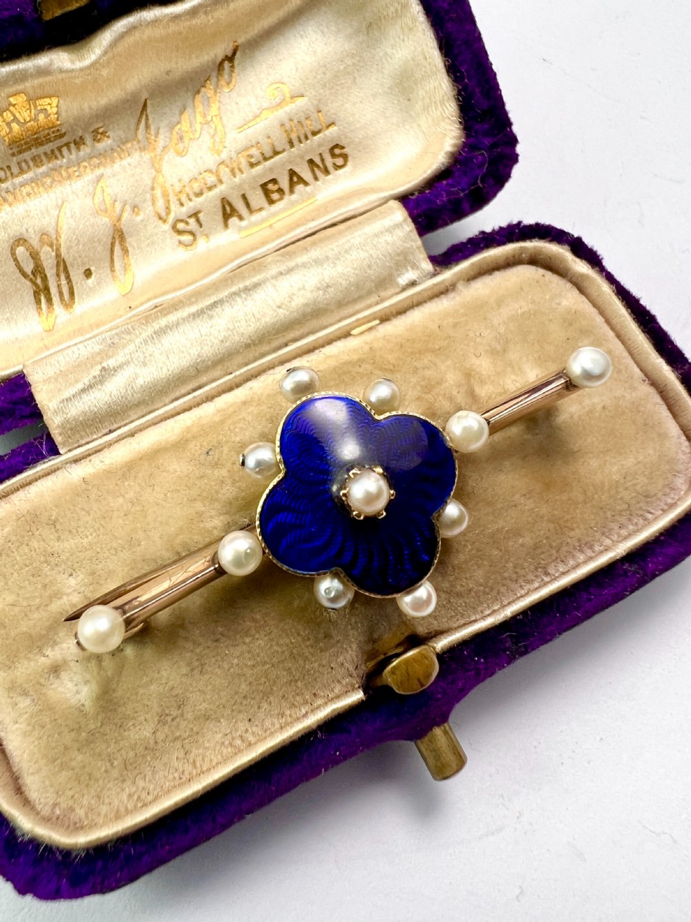 An Edwardian gold bar brooch featuring a central quatrefoil motif decorated in cobalt blue guilloche enamel and surrounded by pearls. View IV