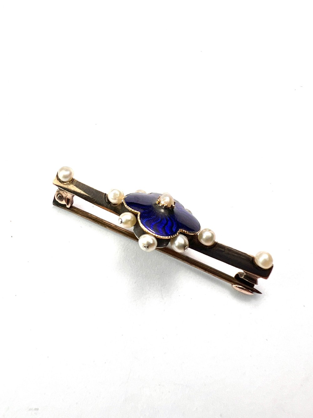 An Edwardian gold bar brooch featuring a central quatrefoil motif decorated in cobalt blue guilloche enamel and surrounded by pearls. View VII